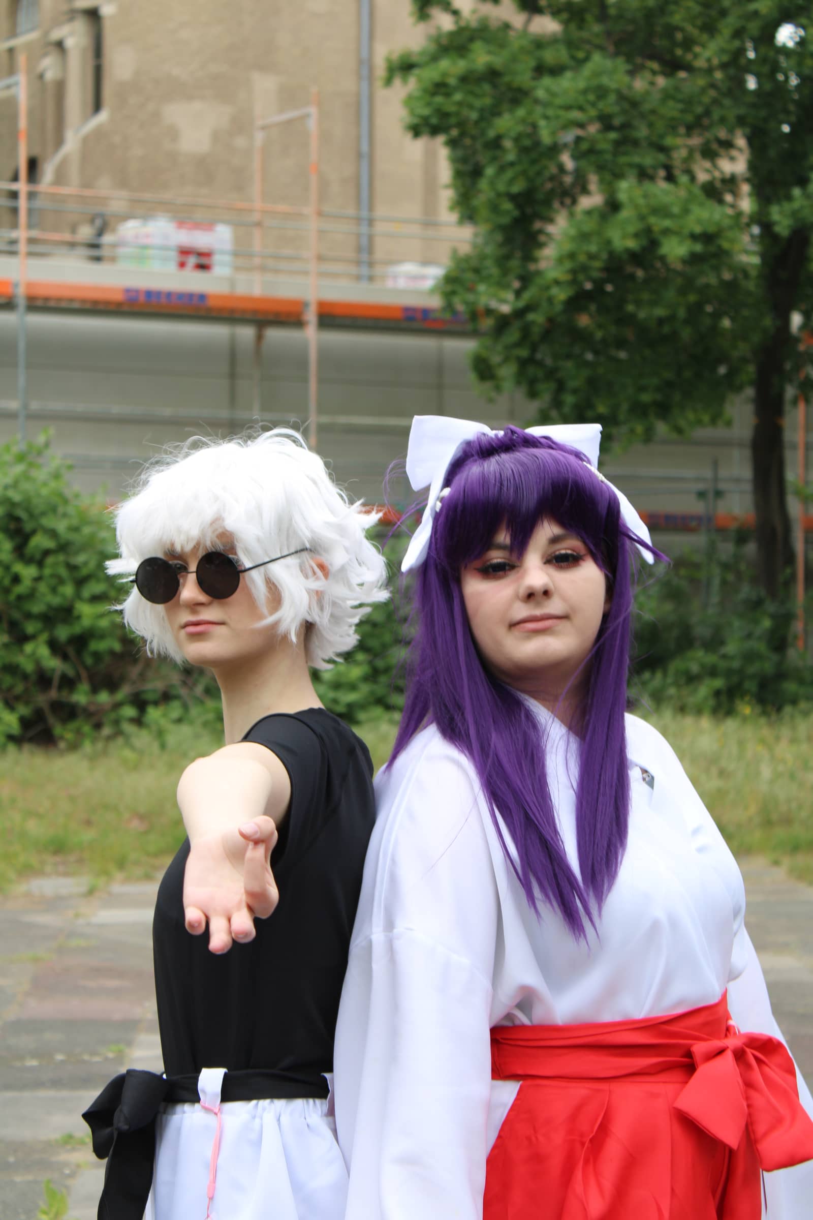 Zwei Cosplayer chillen draußen — silberweiße Perücke trifft Schreinmädchen